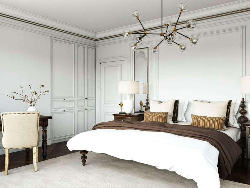 A spacious bedroom featuring the Ophelia Bed in Tobacco by James+James, adorned with white and brown bedding, flanked by two wooden nightstands with lamps. A modern chandelier hangs from the ceiling. A desk with a chair is placed in the corner, and built-in cabinets are along the adjacent wall.