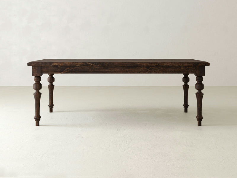 The Allyson Dining Table by James+James stands alone against a plain white background. Crafted from Alder hardwood, this dark wooden table features a rustic design with beautifully carved legs and a smooth rectangular tabletop. Its classic craftsmanship and elegant style give it a timeless and sturdy appearance.