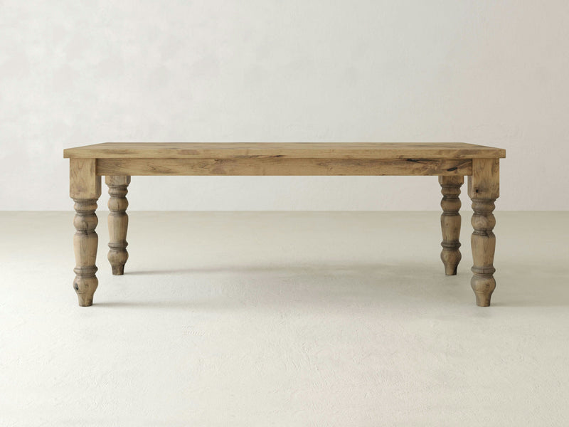 The Baluster Dining Table - Harvest Wheat by James+James is centered against a plain, light-colored background. The rectangular wooden table, with a natural finish, features four turned legs and a simple, rustic design.