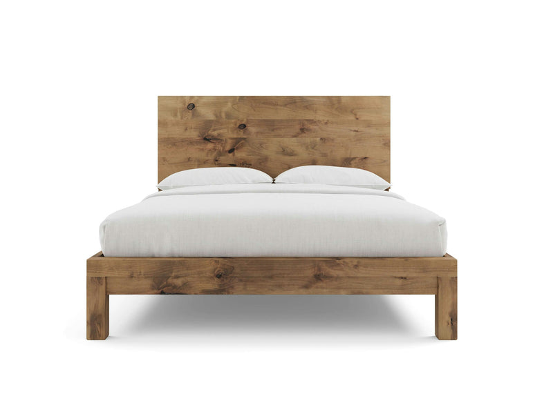 The Sawyer Bed - Harvest Wheat by James+James is shown, featuring a high rectangular headboard with visible wood grain patterns and a natural finish. The wooden bed frame is neatly made with white bedding and two white pillows, showcasing a minimalist and rustic design.