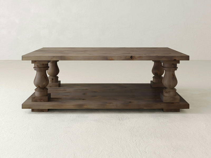 The Vivien Coffee Table - Barn Wood by James+James is a rustic piece with a rectangular top and a lower shelf. It features four ornate, turned legs that connect the top and bottom surfaces, giving it a classic and sturdy appearance. The table boasts a natural, polished wood finish.