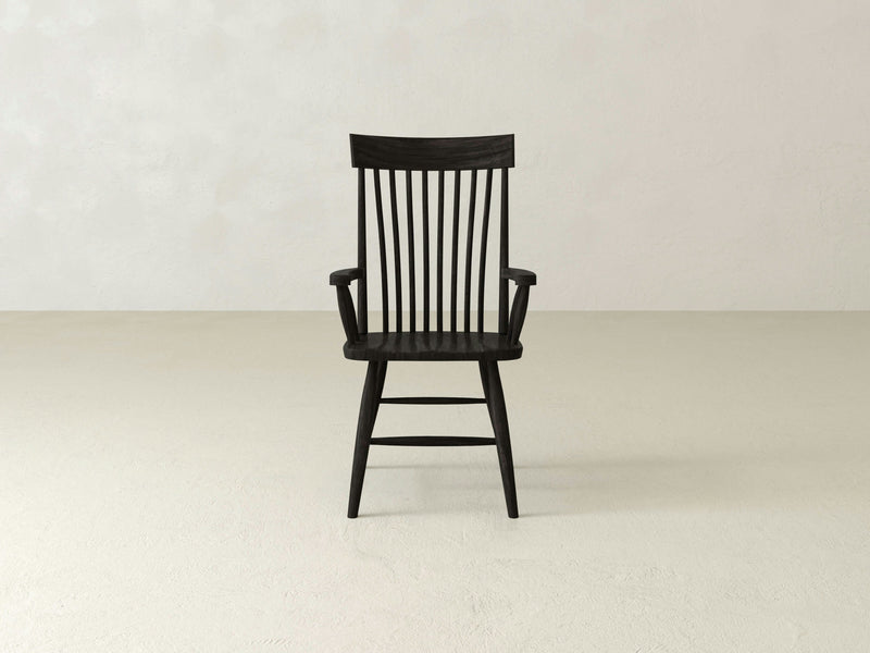 An Eleanor Arm Dining Chair - Charred Ember by James+James, featuring slender vertical slats on the backrest and armrests, is placed against a plain off-white background. The chair, with its minimalist design, rests on four legs with supportive crossbars.