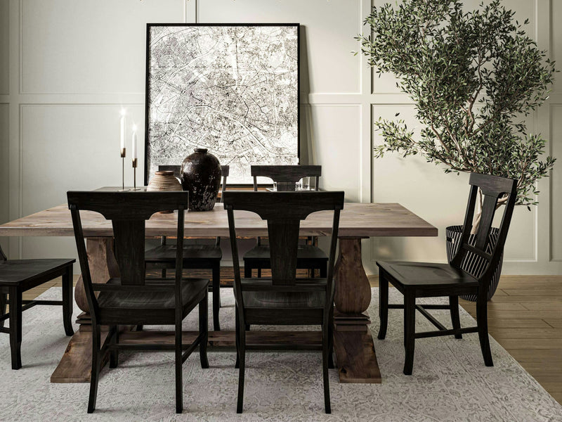 A dining area featuring the Heirloom Expandable Dining Table in Barn Wood by James+James, set with five black chairs. On the table are a couple of tall lit candles, a black vase, and decorative items. Behind the table is a large abstract wall art piece, and a tall green plant is placed in the right corner of the room.