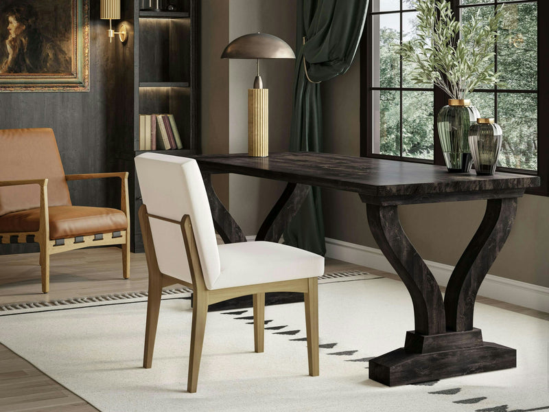 A chic home office with the Vera Desk in Charred Ember by James+James, featuring ornamental legs, a white cushioned chair, a lamp with a gold shade, and two green vases holding greenery. There’s a leather armchair in the corner, a framed painting on the wall, and a large window with green curtains.