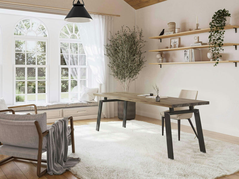 A bright and airy home office with large arched windows features the Fulton Desk in Harvest Wheat from James+James, a wooden desk with black legs. There’s a cushioned window seat and a light rug for added comfort. The space is complemented by a potted tree, minimalistic wooden shelves with decor, and a modern black pendant light.