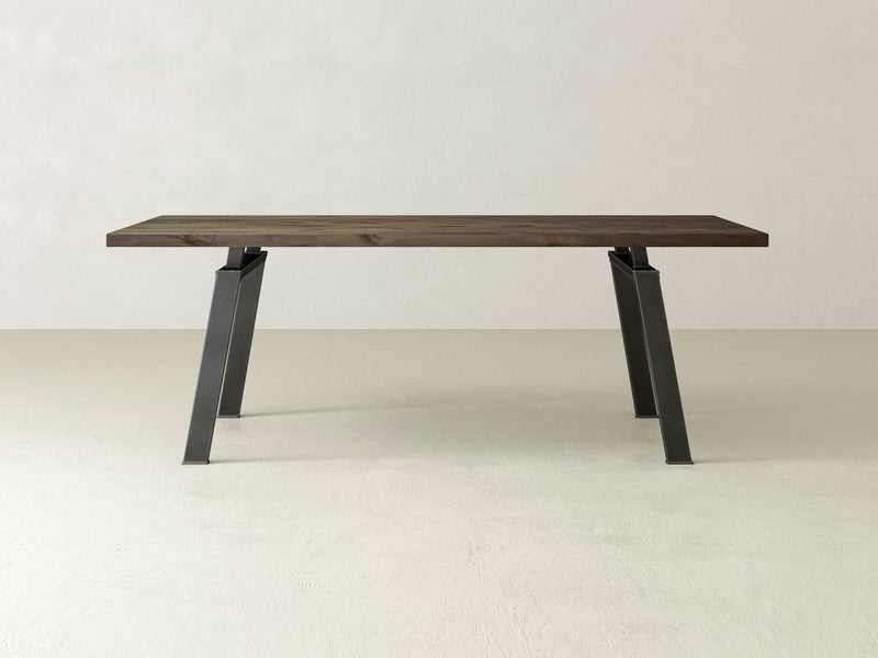 The Fulton Dining Table - Barn Wood by James+James features a minimalist design with a dark brown rectangular top and angular metal legs, set against a plain light-colored background.