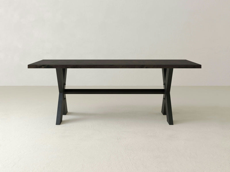 The X-Base Dining Table by James+James is a minimalist rectangular dining table with a modern design and dark wood finish. It boasts a sturdy, solid wood top with simple, clean lines and features two A-frame legs connected by a horizontal support bar. The background is plain and neutral.