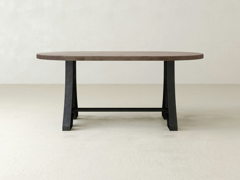 The Wishbone Oval Dining Table - Barn Wood by James+James features a thick, smooth top and sturdy black legs, set against a light, simple background. The table boasts a modern, minimalist design with a sleek and clean appearance.