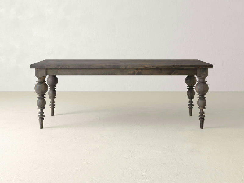 A Bailey Dining Table - Deep Grey from James+James stands against a plain, light-colored background. The table features four intricately carved legs with a classic design and a simple rectangular top.