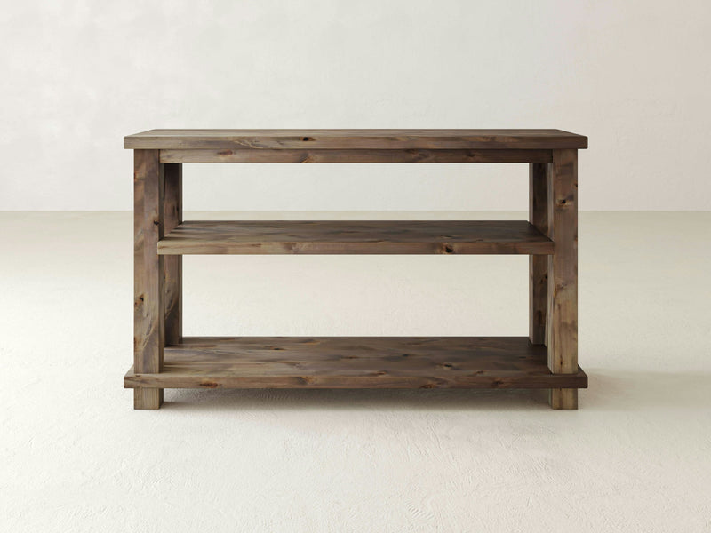 The Carter X Sofa Table by James+James features a minimalistic design crafted from barn wood. It boasts a rectangular top surface, alongside a middle and bottom shelf for ample storage. With its sturdy four-leg construction, this wooden console table combines functionality with clean, simple lines.