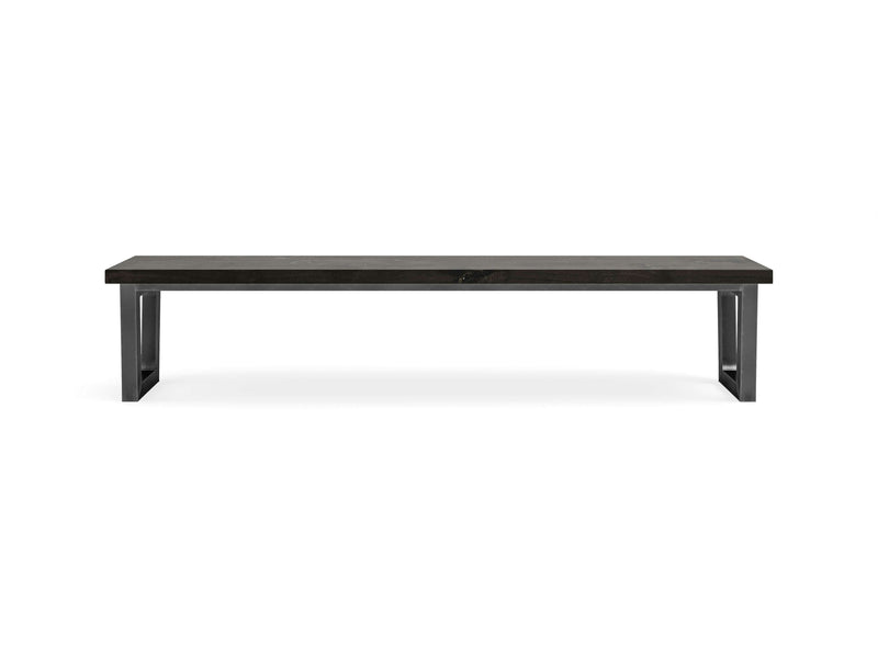 The Trapezoid Bench - Charred Ember by James+James features a modern, minimalist design with a dark, rectangular wooden seat and sturdy black metal legs in a U-shape. The bench is photographed against a plain white background.