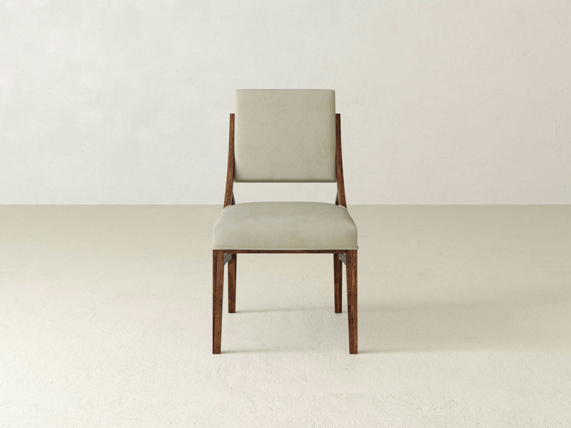 The Quinn Dining Chair - Tuscany by James+James is a minimalist piece featuring a beige cushioned seat and backrest, supported by a wooden frame. It is showcased centrally against a neutral, solid background.