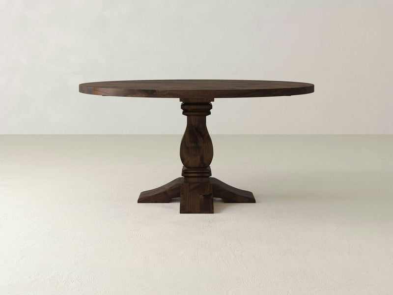 The Heirloom Round Dining Table - Tobacco by James+James features a single central pedestal leg that branches out into four feet. This dark brown wooden table boasts a smooth finish and an elegant, classic design, making it perfect for dining or decor.