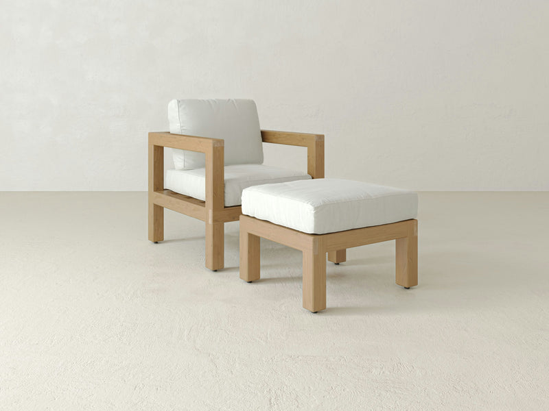 A minimalist scene showcasing the Aria Outdoor Chair and Ottoman by James+James, featuring a wooden outdoor chair with white cushions paired with a matching cushioned ottoman. Both pieces boast a simple, modern design and are set against a plain, light background, perfect for refined outdoor living.