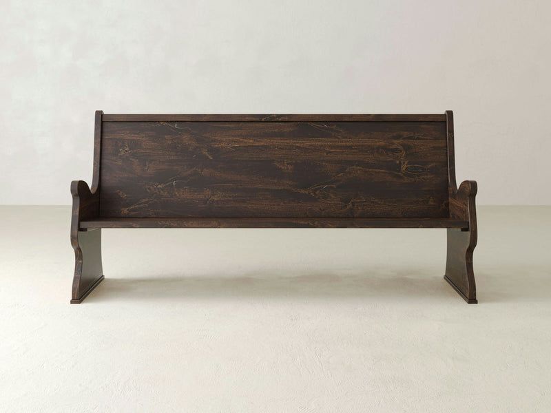 A James+James Rustic Church Pew Bench, crafted from solid hardwood and featuring a high backrest and curved legs, stands against a plain, light-colored wall. This bench offers an antique aesthetic with its rustic, polished finish and straightforward, classic design reminiscent of traditional church seating.