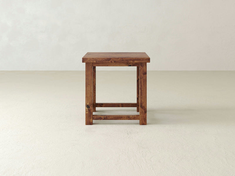 The Carter X Side Table - Tuscany by James+James is a small wooden side table that features a square top and cross-braced legs with a rustic, natural wood finish. Its open design and X-shaped supports on each side provide both sturdiness and style.