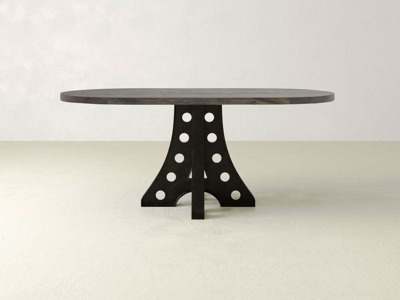 A round wooden table with a dark finish and a unique, sculptural base featuring circular cutout details. The table stands on a light-colored floor against a plain, light-grey wall. 
Product Data: Product Name: Amelia Oval Dining Table - Deep Grey Brand Name: James+James

Rewritten sentence:
The Amelia Oval Dining Table by James+James boasts a deep grey finish and an artistic, sculptural base with circular cutout details. It elegantly stands on a light-colored floor against a plain, light-grey wall.