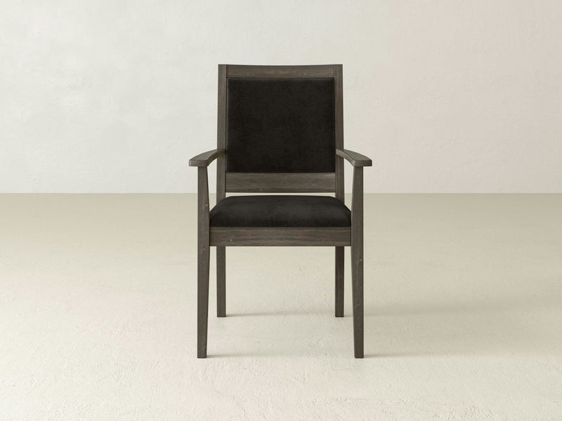 The Gina Arm Dining Chair - Barn Wood by James+James, featuring a dark brown frame and black upholstered seat and backrest, is centered against a plain light-colored background. The chair includes armrests and boasts a simple, modern design.