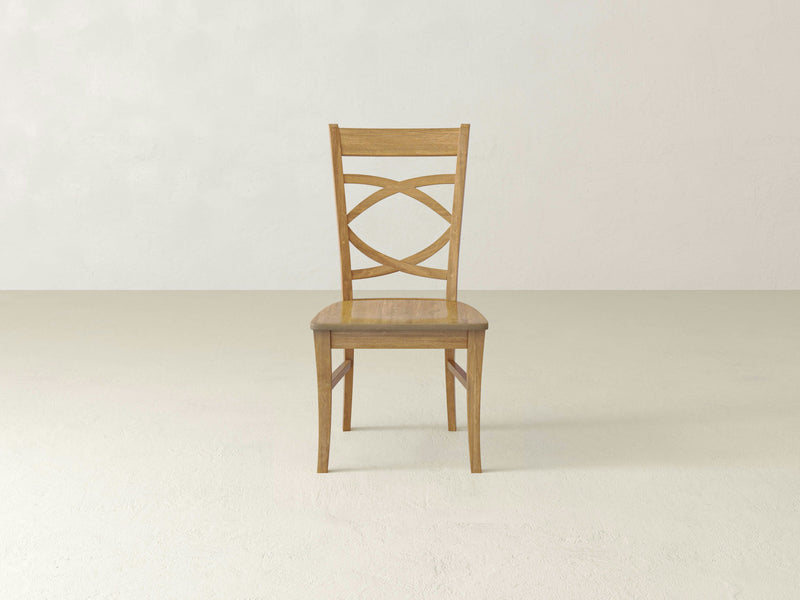 The Ansley Dining Chair - Harvest Wheat by James+James is positioned against a plain, light-colored background. This single wooden chair features a light brown finish, a decorative backrest with an interwoven design, and simple, straight legs. The overall style is minimalist and contemporary.