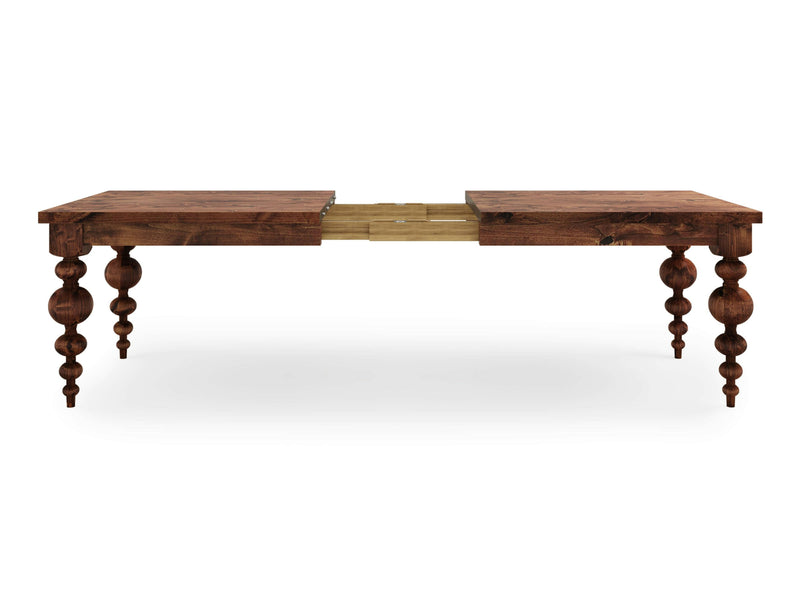 The Olivia Expandable Dining Table - Tuscany by James+James is a wooden dining table showcasing an extension mechanism in the middle. It features intricately carved, spindle-shaped legs and boasts a rich, dark finish. The central section of the table appears to be separated, indicating it's extendable.