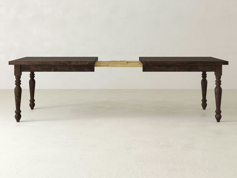 The James+James French Country Expandable Dining Table - Tobacco features a dark wooden finish and turned legs, displayed in an extended position with a leaf section visible in the middle. The neutral background highlights the table's rich finish and timeless design.