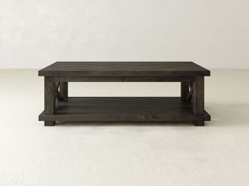 The Carter X Coffee Table - Deep Grey by James+James is a dark wooden, rectangular coffee table that features a lower shelf for additional storage or display. Its simple and minimalist design stands out against a plain, light-colored background.