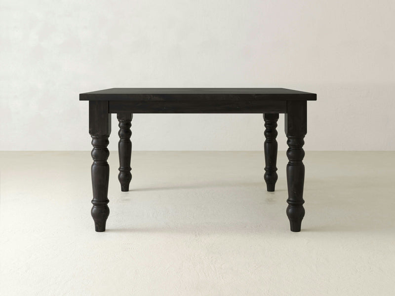 Set against a light-colored floor and plain, light-colored wall, the Baluster Square Dining Table by James+James showcases a handcrafted black wooden tabletop and four ornately carved legs featuring classical turned detailing.