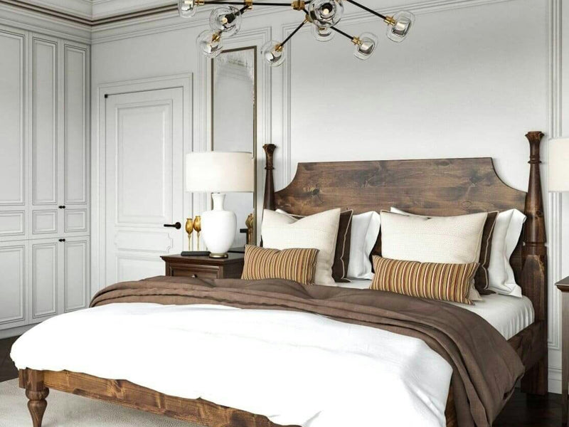 A cozy bedroom featuring the Stella Bed in Tuscany by James+James, adorned with a brown and white bedding set. Decorative pillows and a brown throw blanket accentuate the bed. A wooden nightstand with a white lamp stands beside the bed, while a modern chandelier with exposed bulbs hangs from the ceiling.