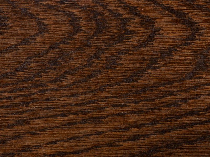 A close-up of the Tobacco on White Oak Sample from James+James showcases its rich brown color with distinctive horizontal grain patterns. The surface texture appears smooth, enhanced by natural variations in the wood that add depth and character.