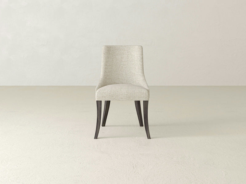 A single deep grey upholstered Willow Dining Chair by James+James, featuring dark wooden legs, is placed against a light grey background. The chair has a curved backrest and a minimalistic design. The setting is simple and uncluttered.