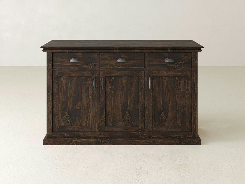 The Nora Buffet by James+James features a dark wooden finish with a flat top. It includes three drawers at the top, each adorned with metal handles, and below these are three larger cabinets, also equipped with metal handles. Its farmhouse style design is both simple and functional, providing ample storage for any dining room or living area. The background is plain.