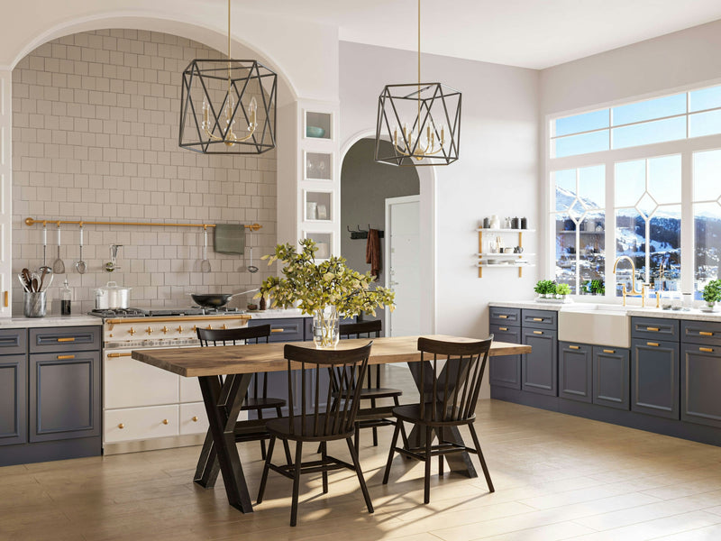 A bright, spacious kitchen with large windows showcasing a snow-covered mountain view features a James+James X-Base Dining Table in Harvest Wheat with black chairs, a tiled backsplash, modern pendant lighting, and blue cabinets with brass handles. A stove and sink are also visible.