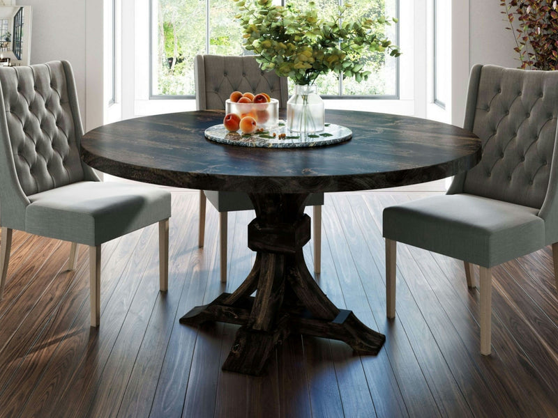 The Violet Round Dining Table in Charred Ember by James+James is set with a glass vase filled with greenery and a plate of peaches. Surrounding the table are four tufted grey chairs with white legs. The room features wood flooring and large windows that let in natural light.