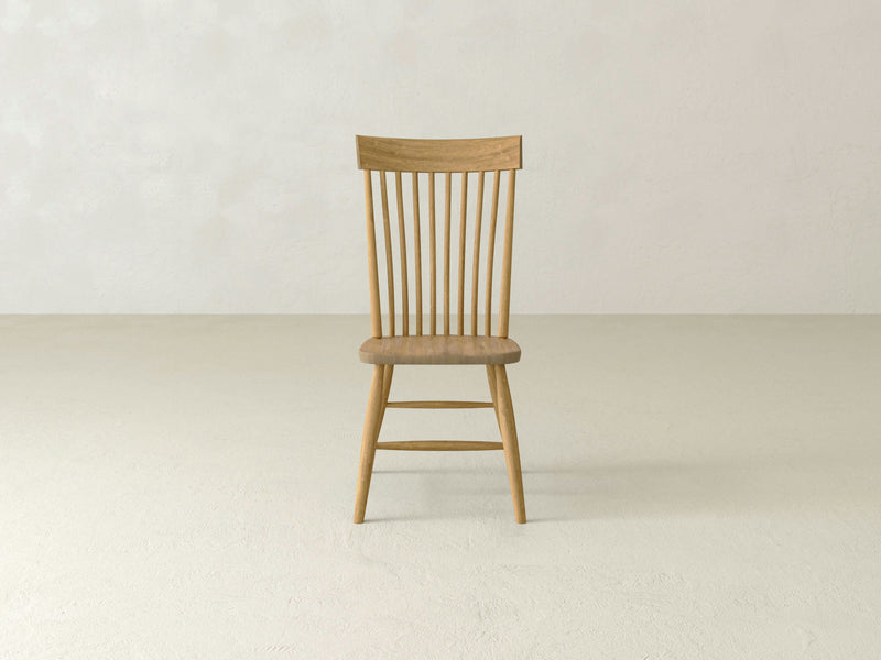 An Eleanor Side Dining Chair - Harvest Wheat by James+James with a simple, minimalist design against a plain, light-colored background. The chair features a spindle backrest and four straight legs. The natural wood grain is visible, highlighting its sturdy and well-crafted build.