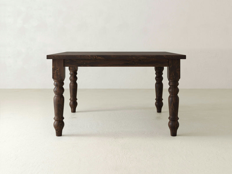 The Baluster Square Dining Table - Tobacco by James+James stands on four intricately carved legs. The table is set against a plain, light-colored background, highlighting its vintage and sturdy design.