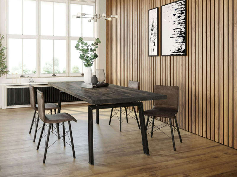 A modern dining room with the Fulton Dining Table in deep grey by James+James and four brown chairs on a light wooden floor. The room features a wall adorned with vertical wooden slats, two abstract paintings, a window allowing natural light, and a decorative potted plant on the table.