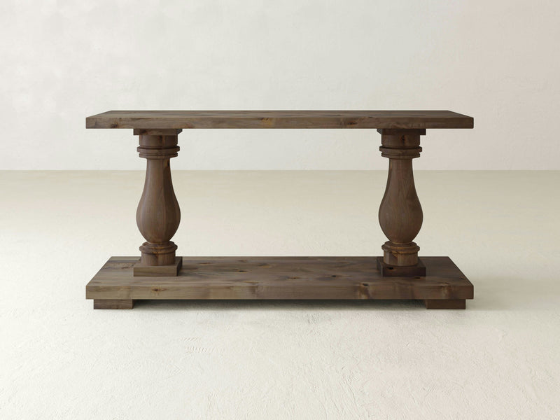 Introducing the Vivien Sofa Table - Barn Wood by James+James. This rustic wooden console table boasts a natural finish and features a rectangular top supported by two intricately carved, turned legs. The legs are connected to a solid rectangular base, creating a piece that exudes both simplicity and elegance.