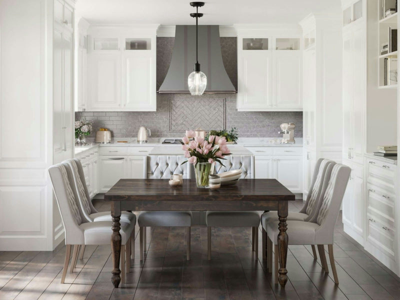 A modern, bright kitchen showcases a white color scheme with light grey accents. At the center, you'll find the James+James French Country Square Dining Table in Tobacco, complemented by four grey-upholstered chairs. A vase filled with pink flowers adds a vibrant touch on the table. The backdrop features white cabinetry and sleek stainless steel appliances.