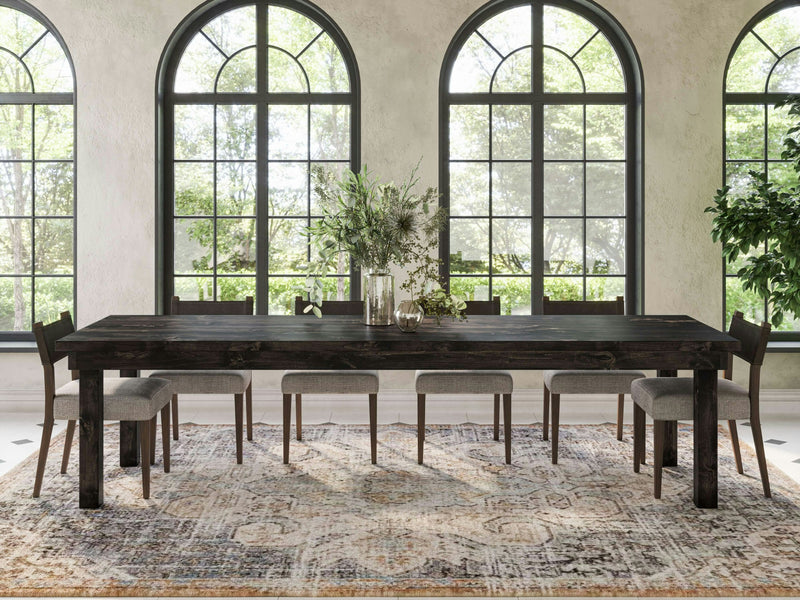 The Farmhouse Expandable Dining Table - Charred Ember by James+James features a dark, textured surface with subtle vertical lines and a faint, irregular lighter mark toward the center. The overall appearance evokes the look of natural wood, with variations in shading and color.