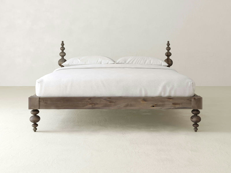 The Ophelia Bed - Barn Wood by James+James, featuring intricately turned bedposts and legs, is centered against a plain white background. The bed is adorned with white bedding, including two pillows and a white sheet, creating a minimalist and elegant look.