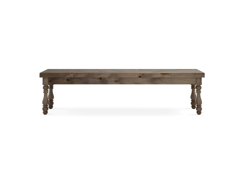 The Annli Bench - Barn Wood by James+James features a rectangular seat and four turned legs. It boasts a rustic finish and straightforward design, highlighting the natural grain of the wood. The legs include decorative carvings that add a touch of elegance. The bench is photographed against a plain white background.