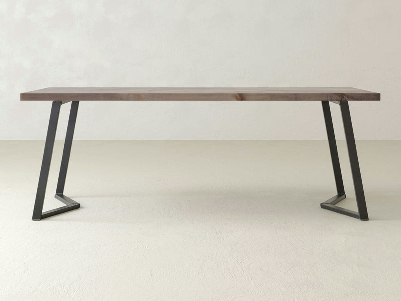 The Arkwright Desk - Barn Wood by James+James is a modern rectangular wooden table featuring a flat surface and slanted black metal legs. The desk is showcased against a plain, light-colored background.