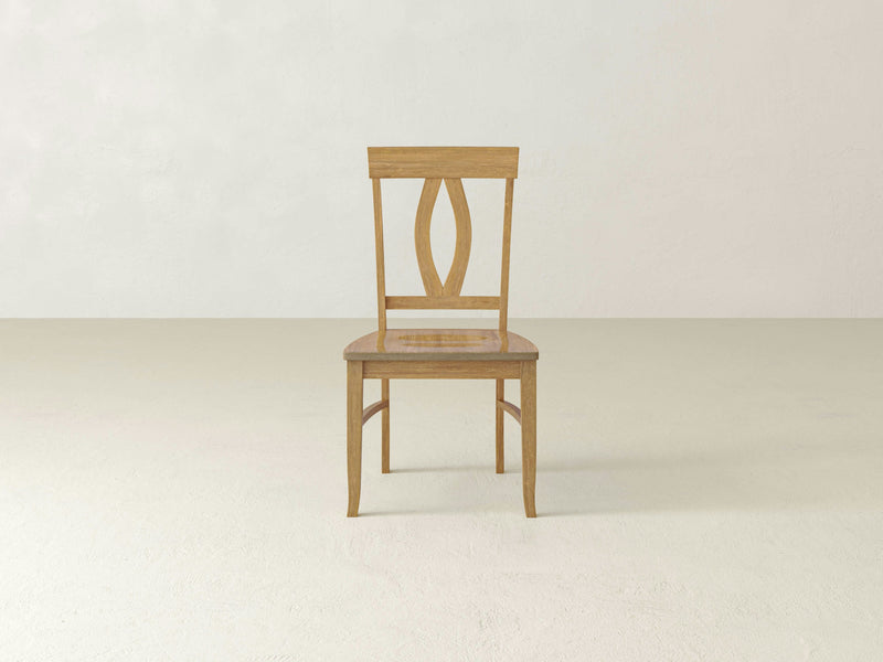 Introducing the Elizabeth Dining Chair - Harvest Wheat from James+James: a wooden chair with a square seat and a curved backrest featuring a vertical slat design. This chair boasts a simple, natural finish and stands on four sturdy legs. It is positioned at an angle, revealing both the side and back against a plain white background.