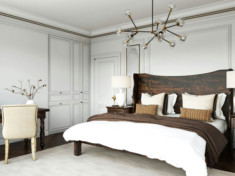 Modern bedroom with the Harlow Bed in Tobacco featuring white and brown bedding. The room includes white paneled walls, a chandelier with exposed bulbs, a desk with a beige chair, and two bedside tables with table lamps. A branch decorates the desk.