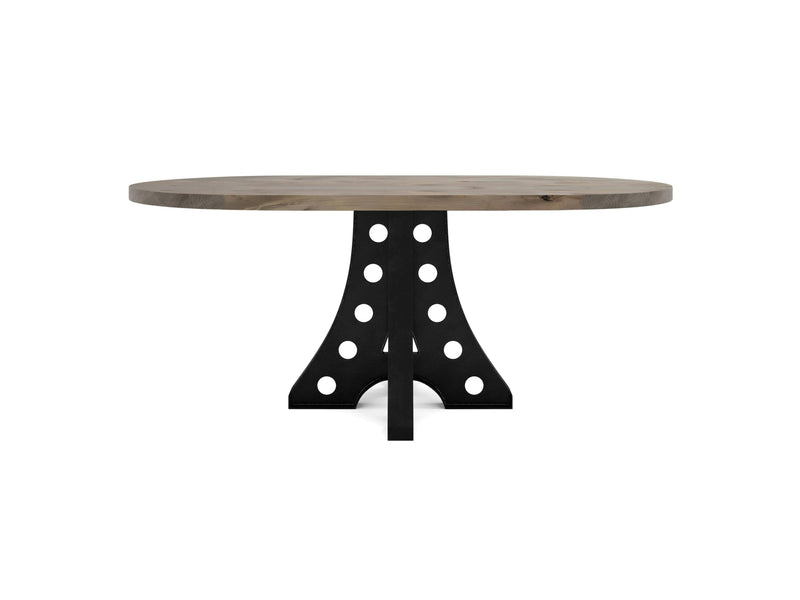 The Amelia Oval Dining Table by James+James has a thick tabletop and a distinctive black pedestal base featuring circular cutout patterns. The design is modern with an industrial flair.