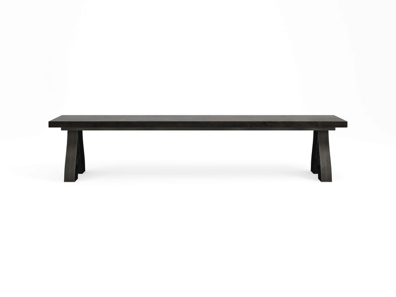 The Wishbone Bench - Charred Ember by James+James is a minimalist, elongated dark wooden bench with a rectangular top and robust, angled legs. Exhibiting clean, straight lines and a modern design, this piece is ideal for both indoor and outdoor use. The plain white background highlights the bench's simple elegance.