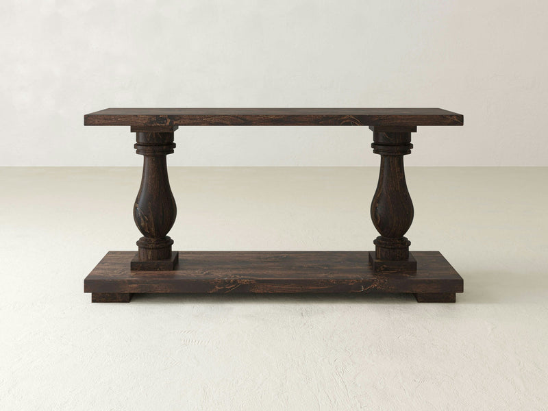 The Vivien Sofa Table in Tobacco by James+James features a wooden, rectangular tabletop and base connected by two ornate, carved baluster-style legs. Its simple and elegant design is perfect for various home decor styles.