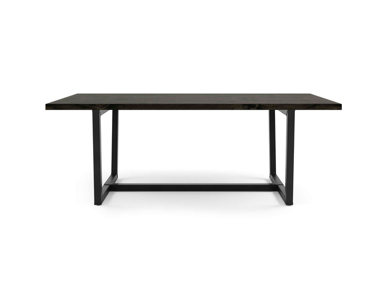 The Trapezoid Dining Table - Charred Ember by James+James is a rectangular, dark-colored wooden table with black metal legs and a minimalist design. Centered on a white background, the table showcases its simple and modern aesthetic.