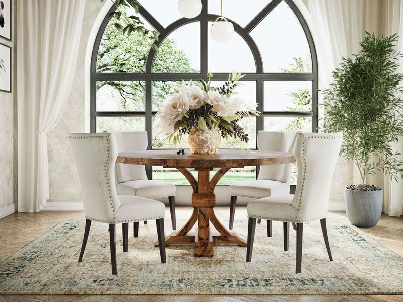 A dining room with a Violet Round Dining Table - Tuscany by James+James, surrounded by four upholstered chairs. The table features a floral centerpiece. A large arched window with white curtains provides a view of lush greenery. A potted plant sits to the right, and a patterned rug covers the floor.