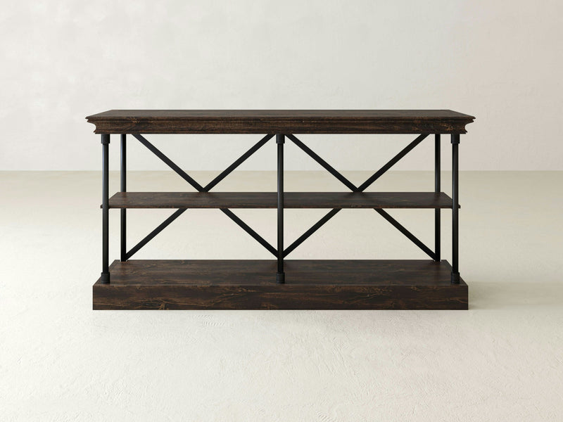 The Annie Shelf by James+James is a dark brown wooden console table featuring two lower shelves, supported by black metal X-cross frames on the sides and back, all set against a plain light-colored background. This table exhibits handcrafted beauty with its classic, minimalist design.